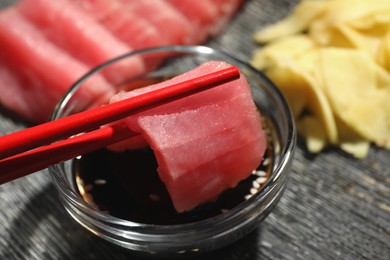 Photo of Dipping tasty sashimi (piece of fresh raw tuna) into soy sauce at black table, closeup