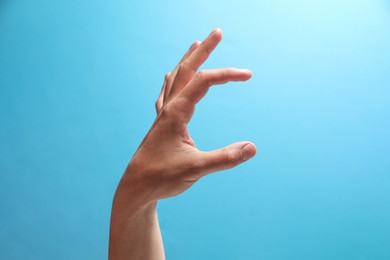 Man holding something in hand on light blue background, closeup