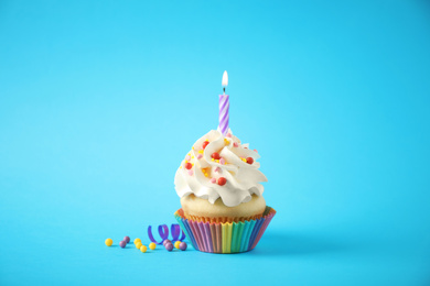 Photo of Delicious birthday cupcake with candle on light blue background