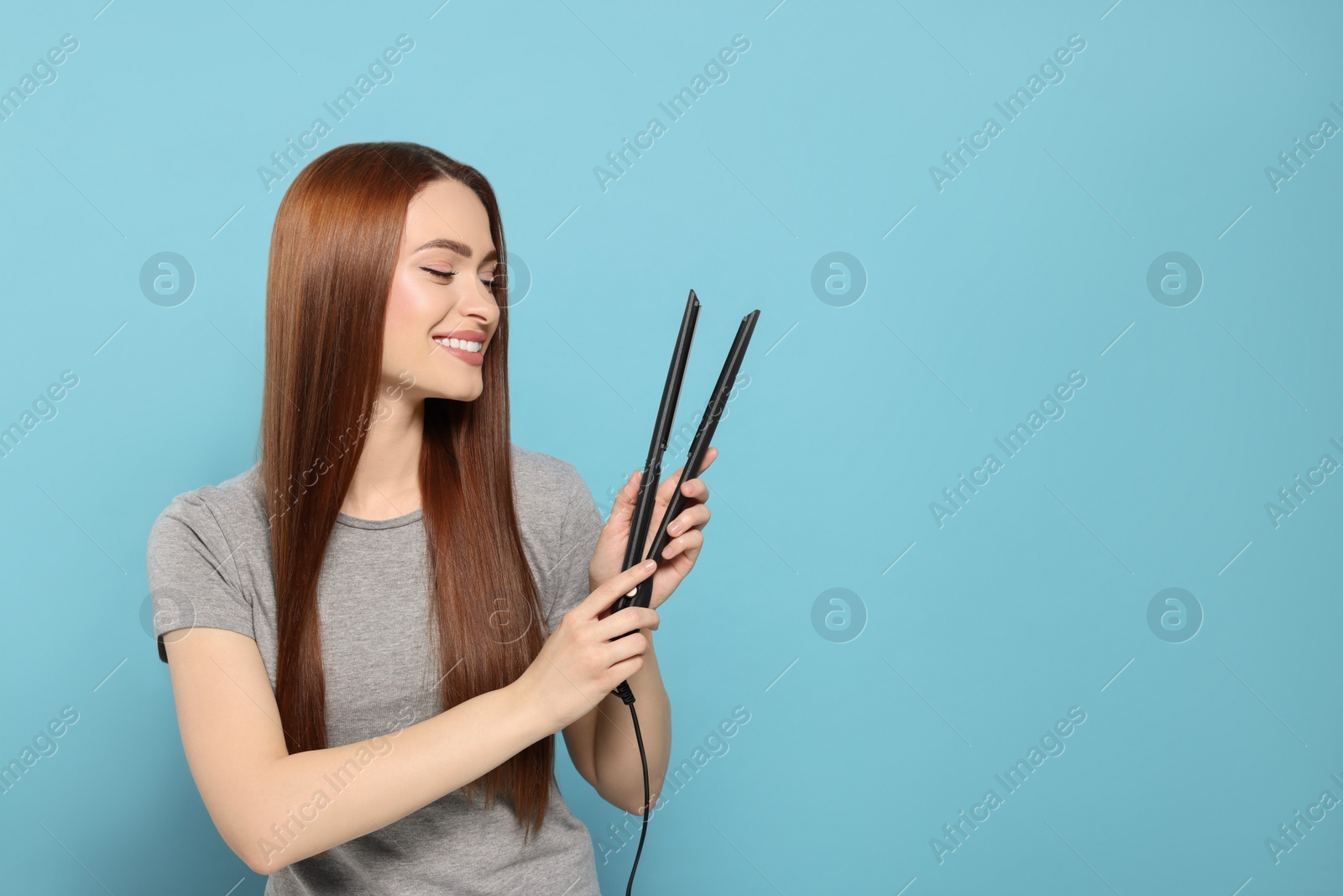 Photo of Beautiful woman with hair iron on light blue background, space for text