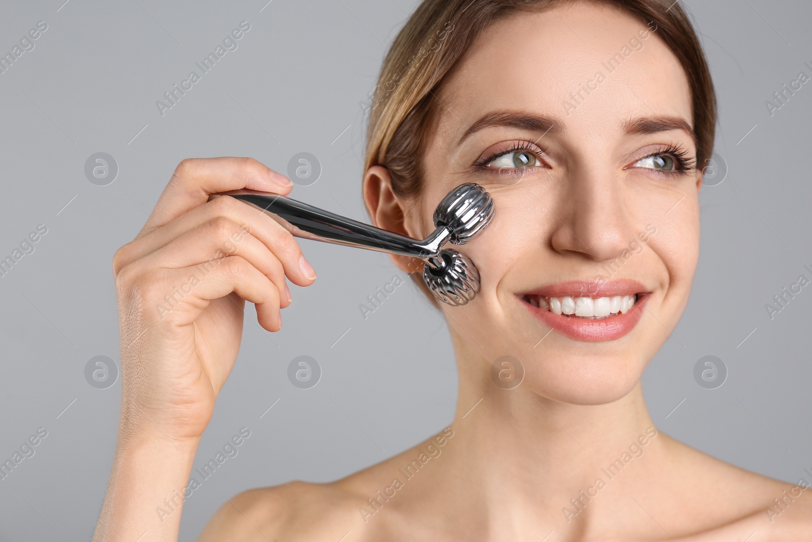 Photo of Young woman using metal face roller on light grey background