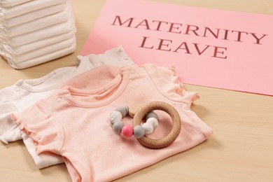 Photo of Baby clothes, toy, diapers and note with text Maternity Leave on wooden table