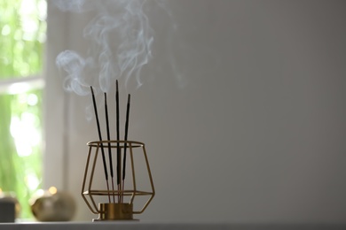 Photo of Incense sticks smoldering on table in room. Space for text