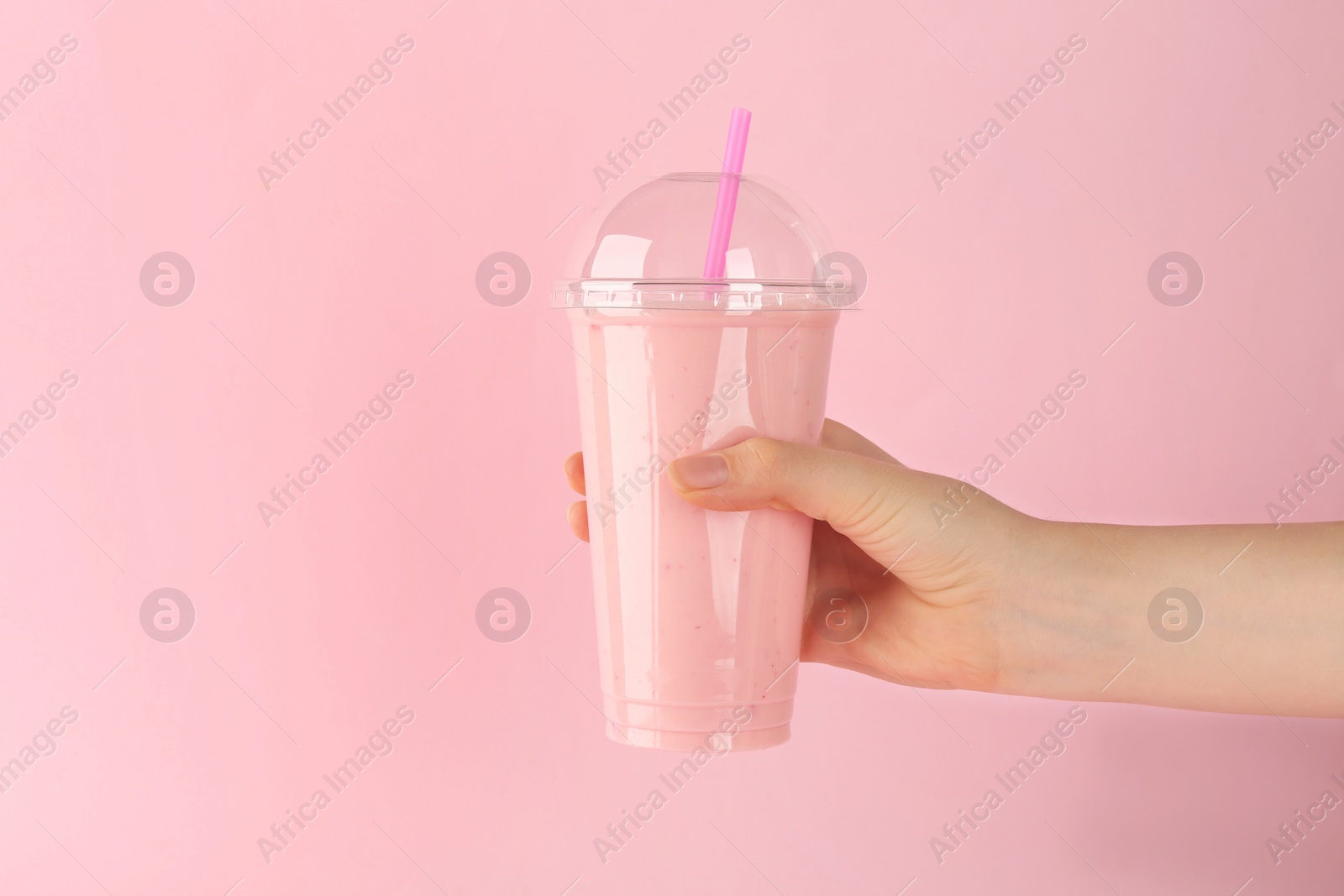 Photo of Woman holding plastic cup of tasty smoothie on pink background, closeup