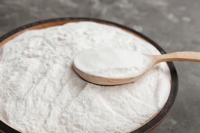 Photo of Bowl and spoon with baking soda on gray table, closeup