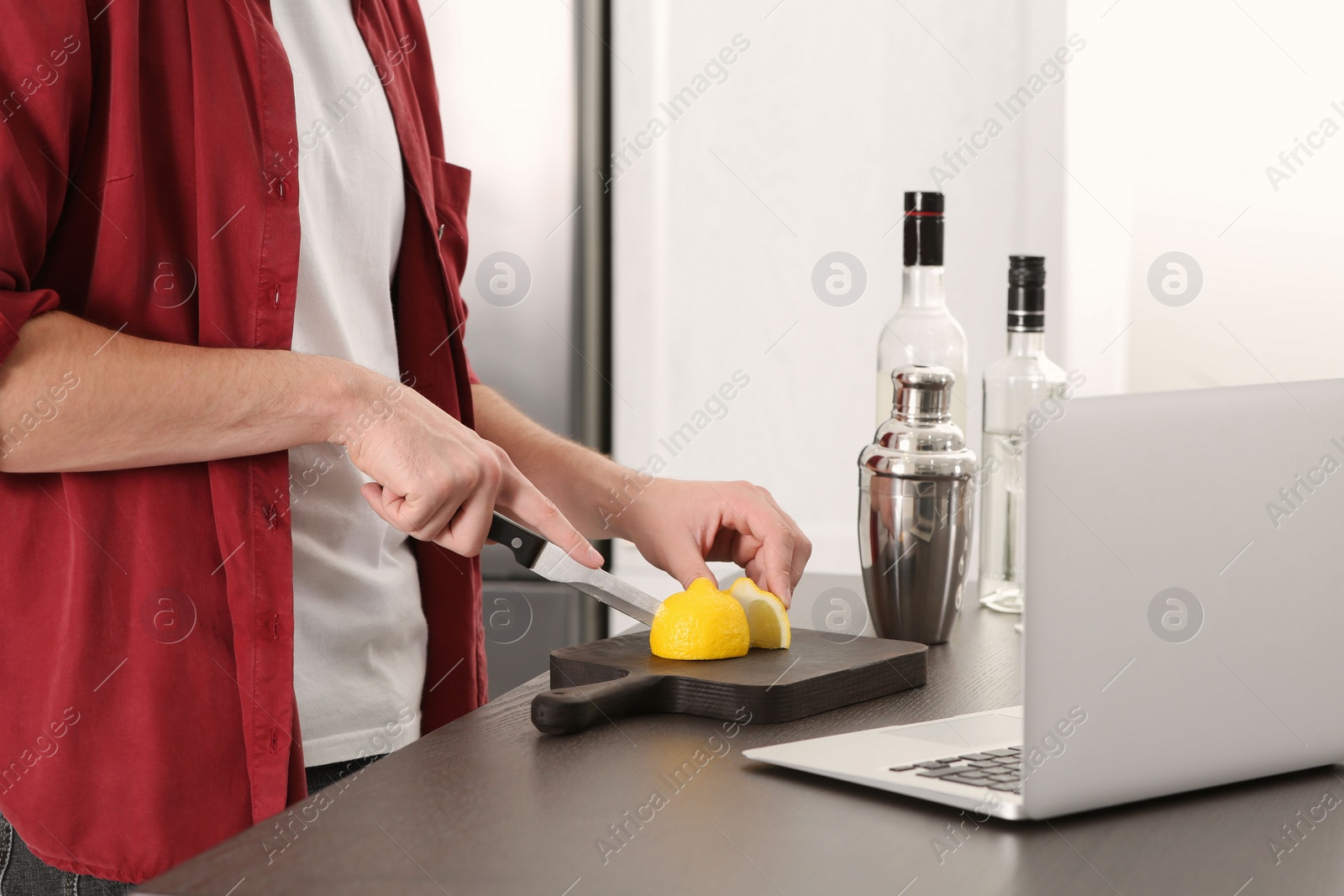 Photo of Man learning to make cocktail with online video on laptop at table in kitchen, closeup. Time for hobby