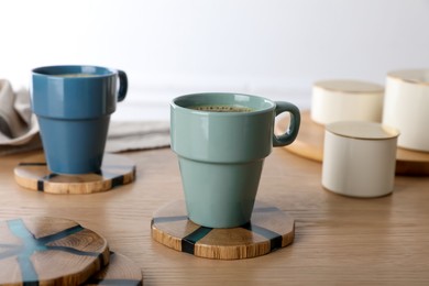Mugs of hot drink with stylish cup coasters on wooden table