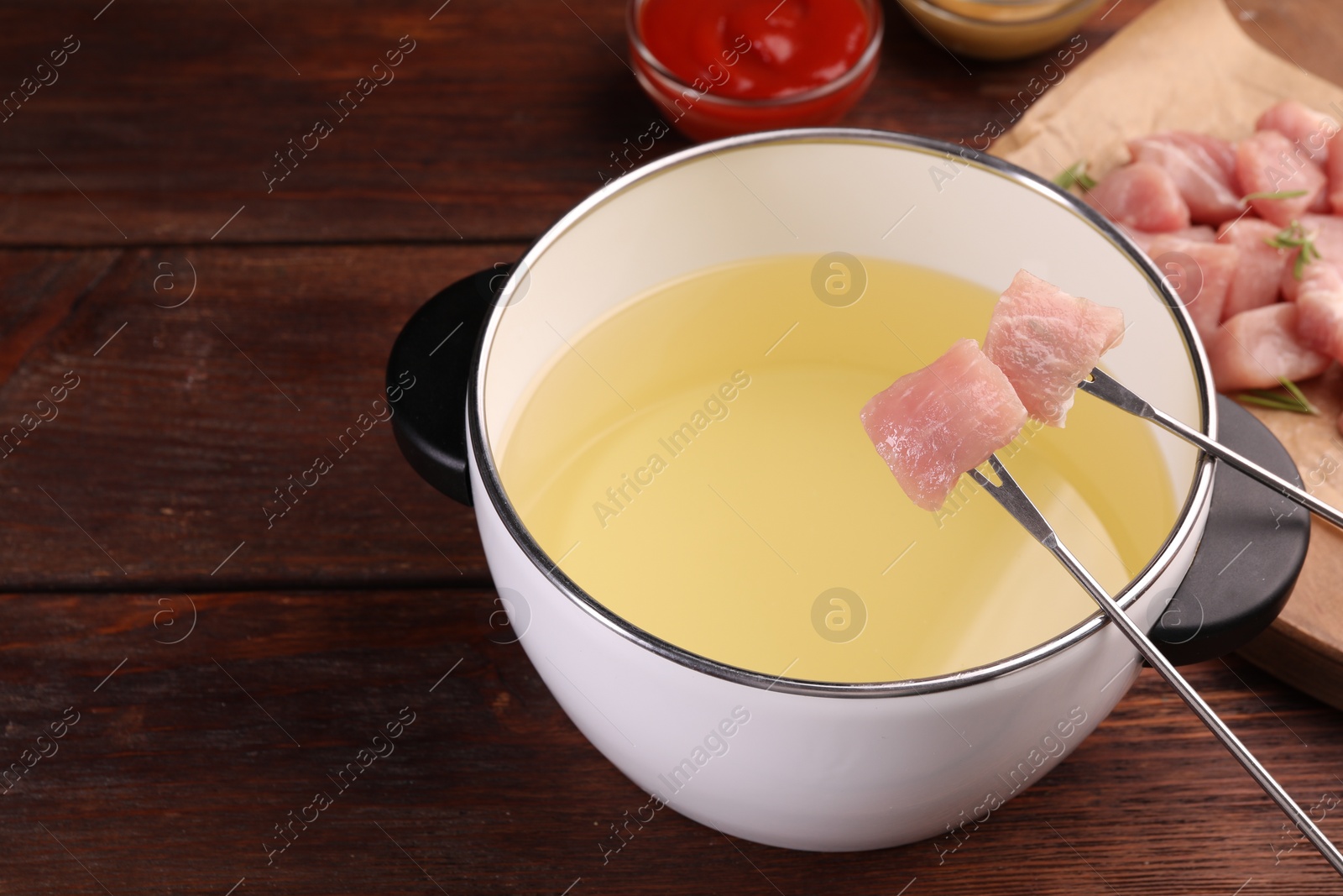 Photo of Fondue pot, forks and pieces of raw meat on wooden table, space for text