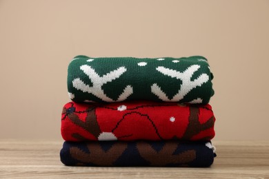 Photo of Stack of different Christmas sweaters on wooden table against beige background