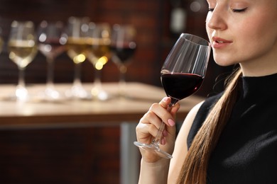 Photo of Beautiful woman with glass of red wine against blurred background, space for text