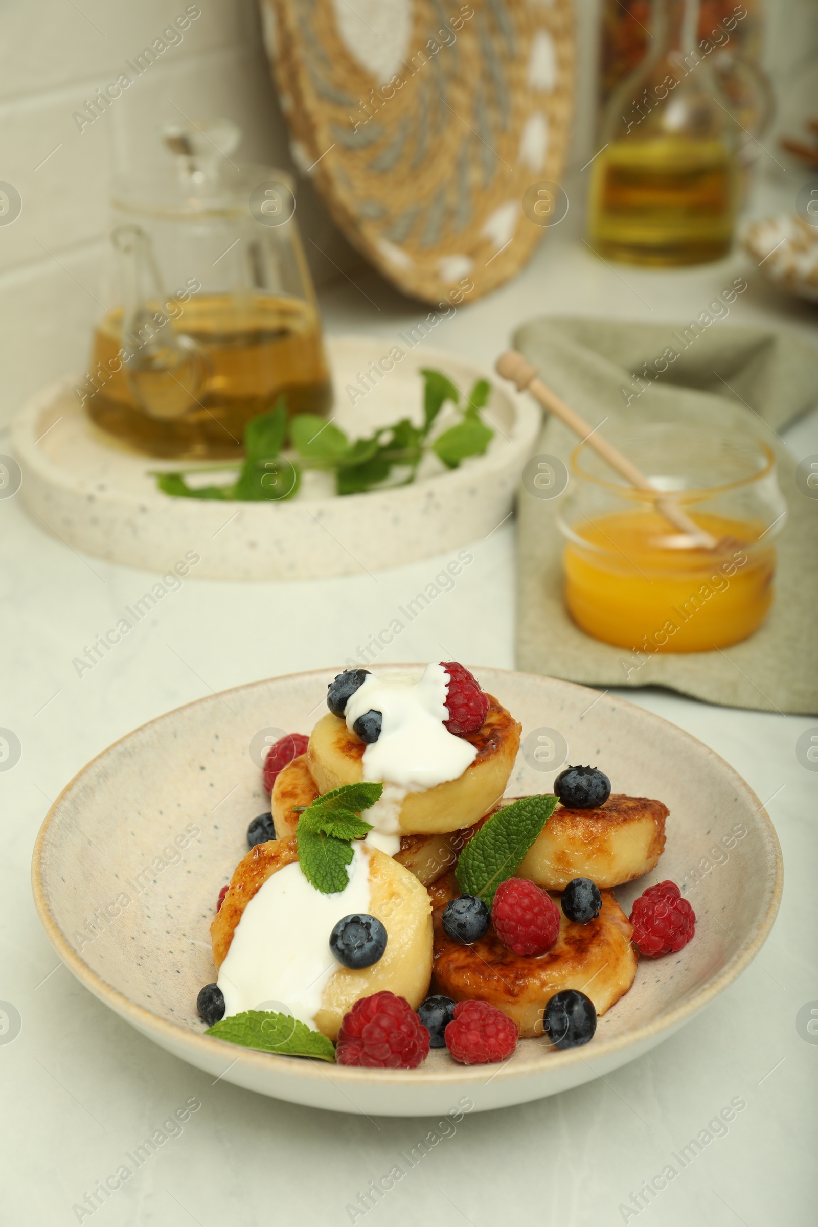 Photo of Delicious cottage cheese pancakes with fresh raspberries, sour cream and mint on white countertop