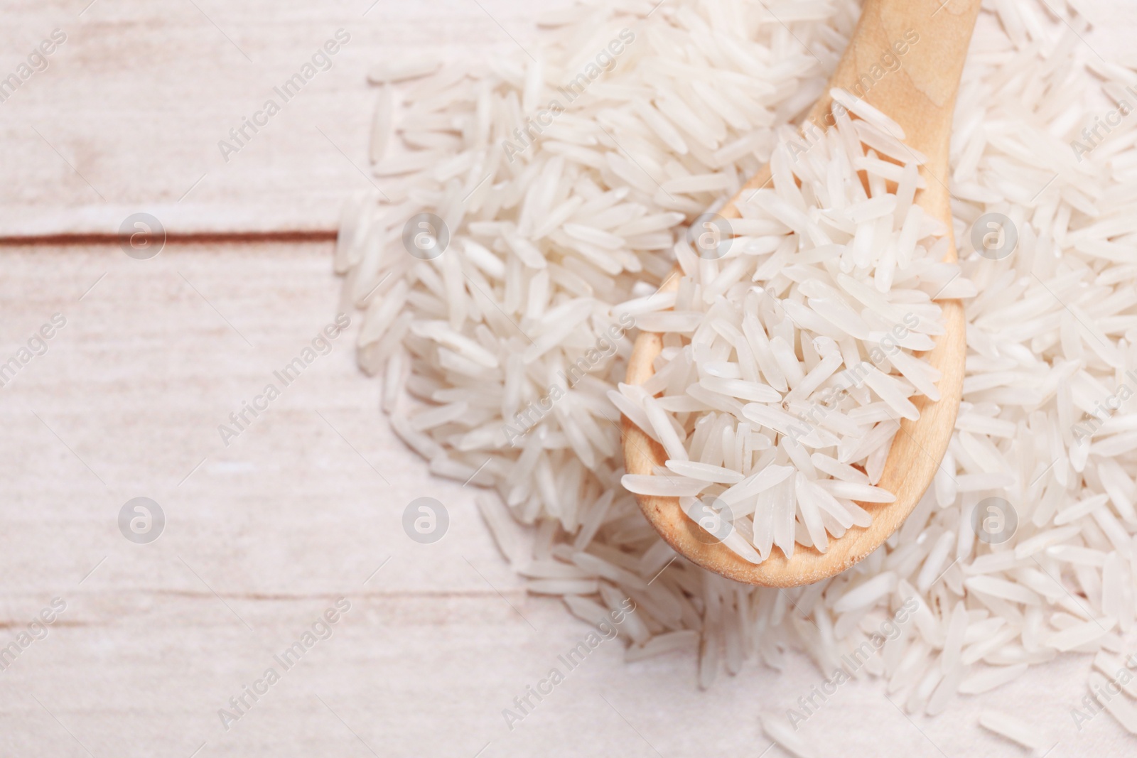 Photo of Raw basmati rice and spoon on white wooden table, top view. Space for text