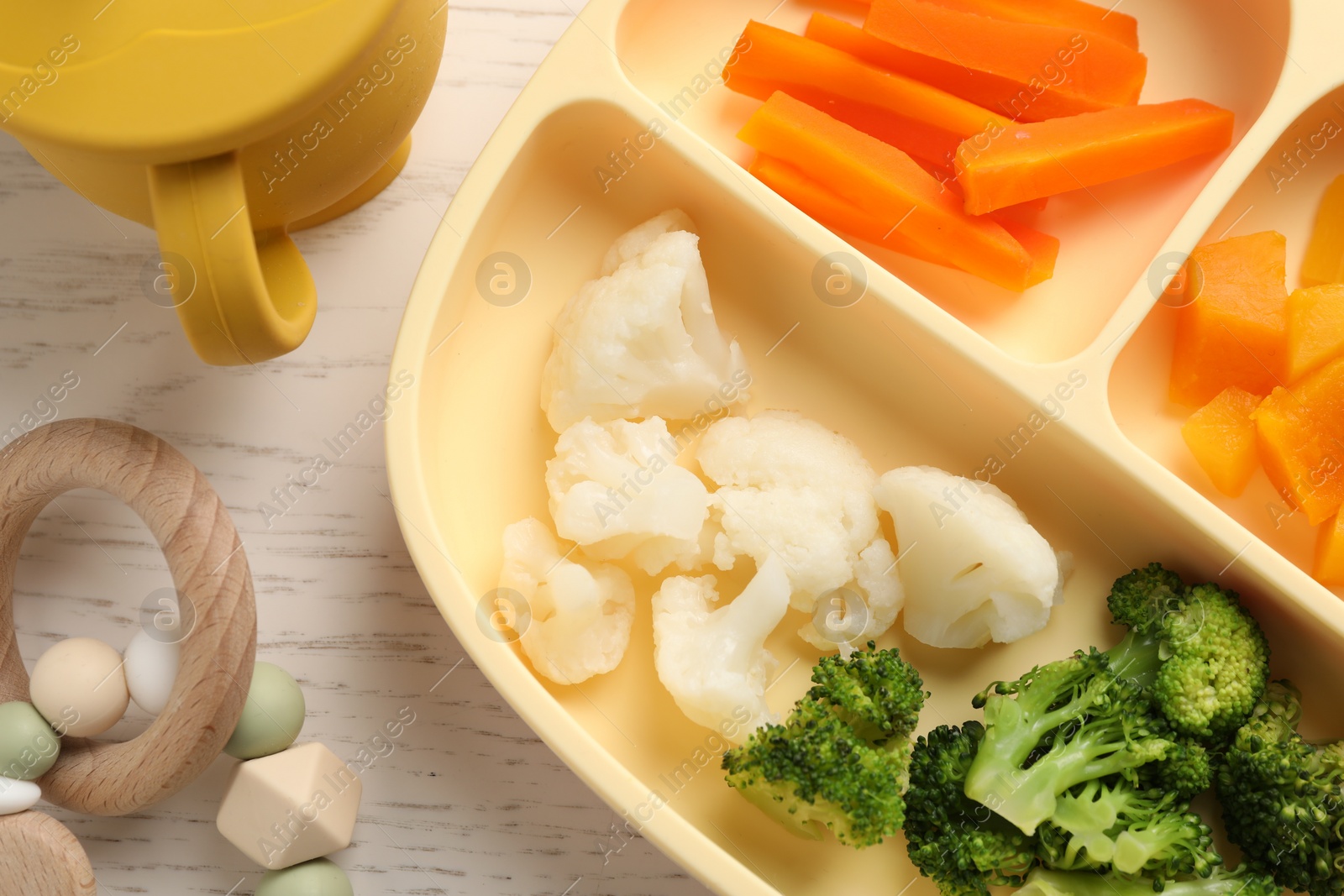 Photo of Baby food. Section plate with different vegetables on white wooden table, flat lay