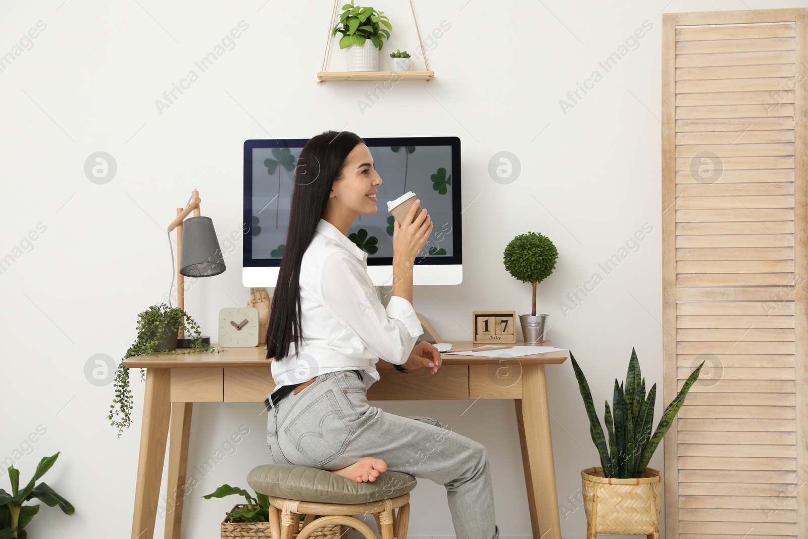 Photo of Young woman with cup of drink at table in room. Home office