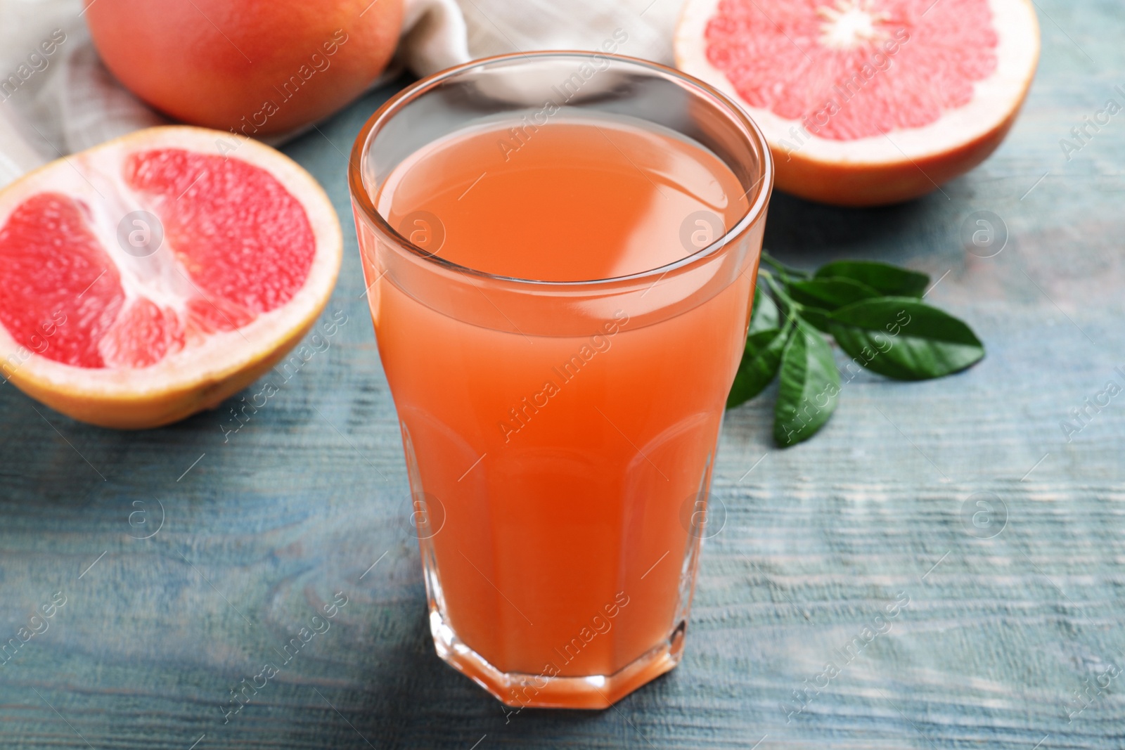 Photo of Tasty freshly made grapefruit juice on blue wooden table, closeup