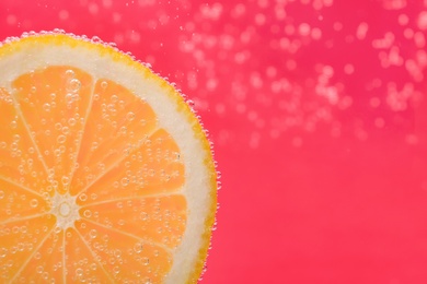 Slice of lemon in sparkling water on pink background, closeup with space for text. Citrus soda