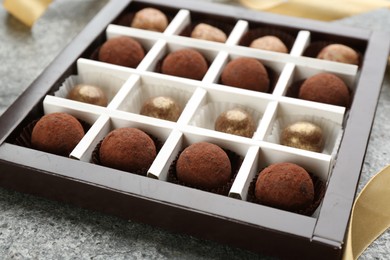 Different delicious chocolate candies in box on grey table, closeup