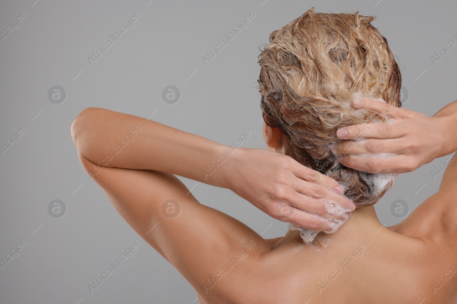 Photo of Woman washing hair on light grey background, back view. Space for text