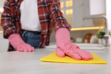 Photo of Woman cleaning white marble table with microfiber cloth in kitchen, closeup