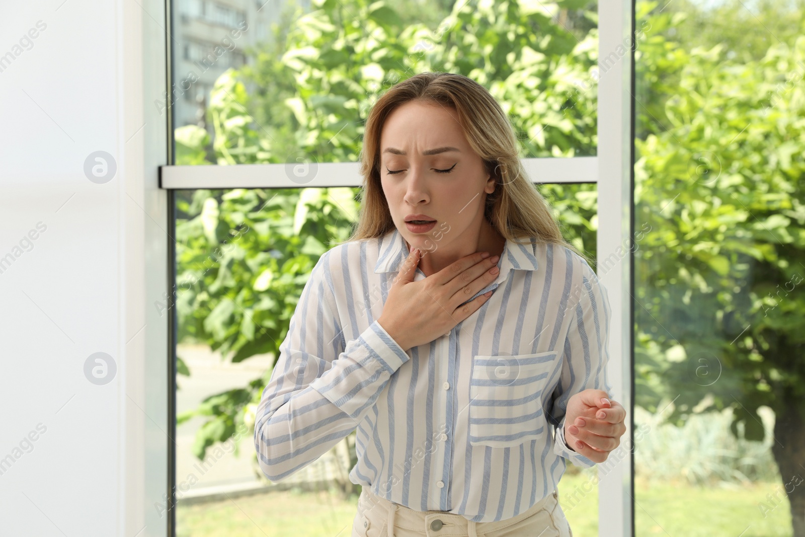 Photo of Young woman suffering from pain during breathing near window