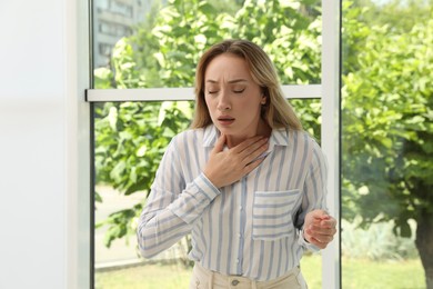 Photo of Young woman suffering from pain during breathing near window