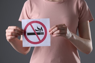 Woman holding card with no smoking sign on gray background, closeup