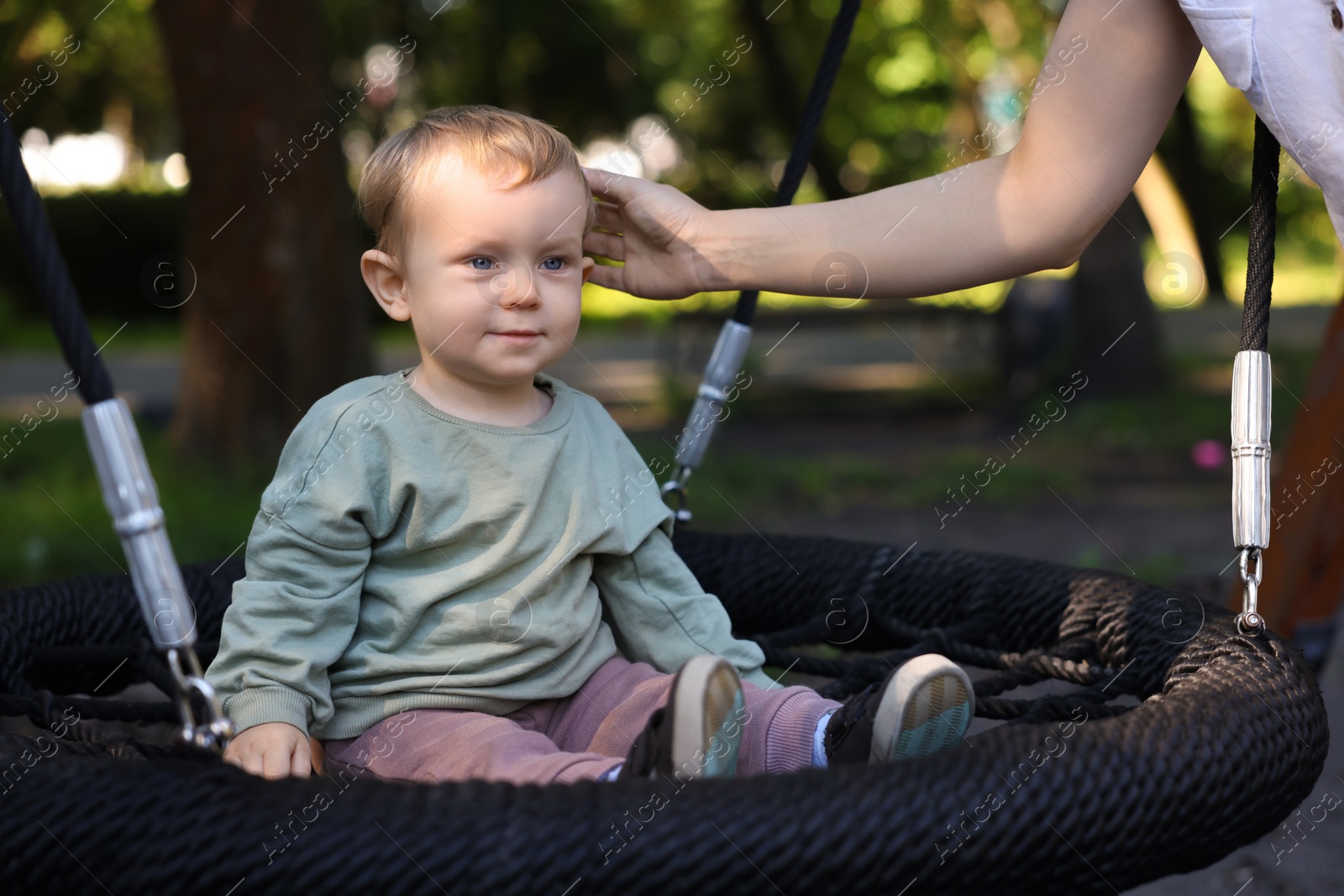 Photo of Nanny and cute little boy on swing outdoors