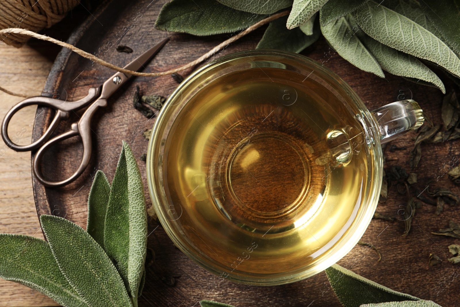 Photo of Cup of sage tea and green leaves on wooden tray, top view