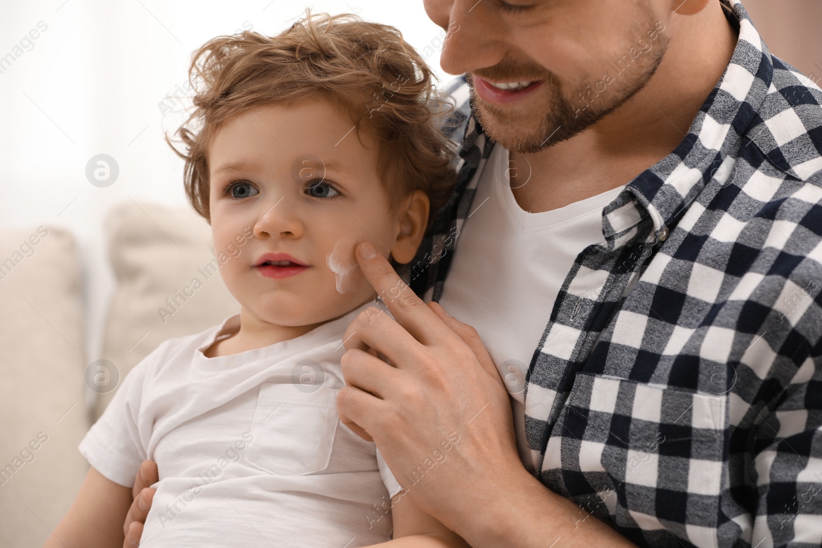 Photo of Father applying ointment onto his son`s cheek indoors