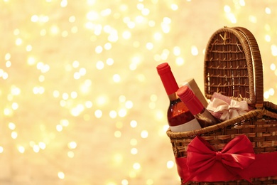 Photo of Festive basket with bottles of wine and gifts against blurred lights. Space for text