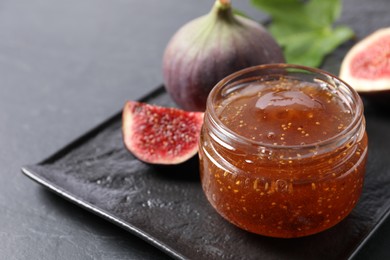 Photo of Jar of tasty fig jam and fresh fruits on black table, closeup. Space for text