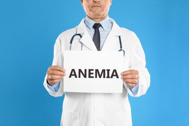 Image of Doctor holding sign with word ANEMIA on blue background, closeup