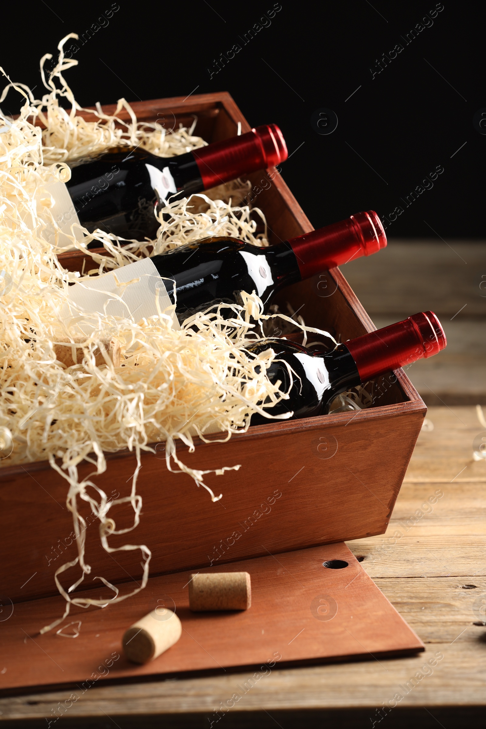 Photo of Box with wine bottles on wooden table against black background