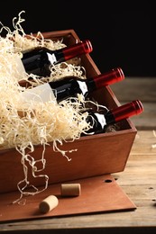 Photo of Box with wine bottles on wooden table against black background