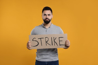 Photo of Man holding cardboard banner with word Strike on orange background