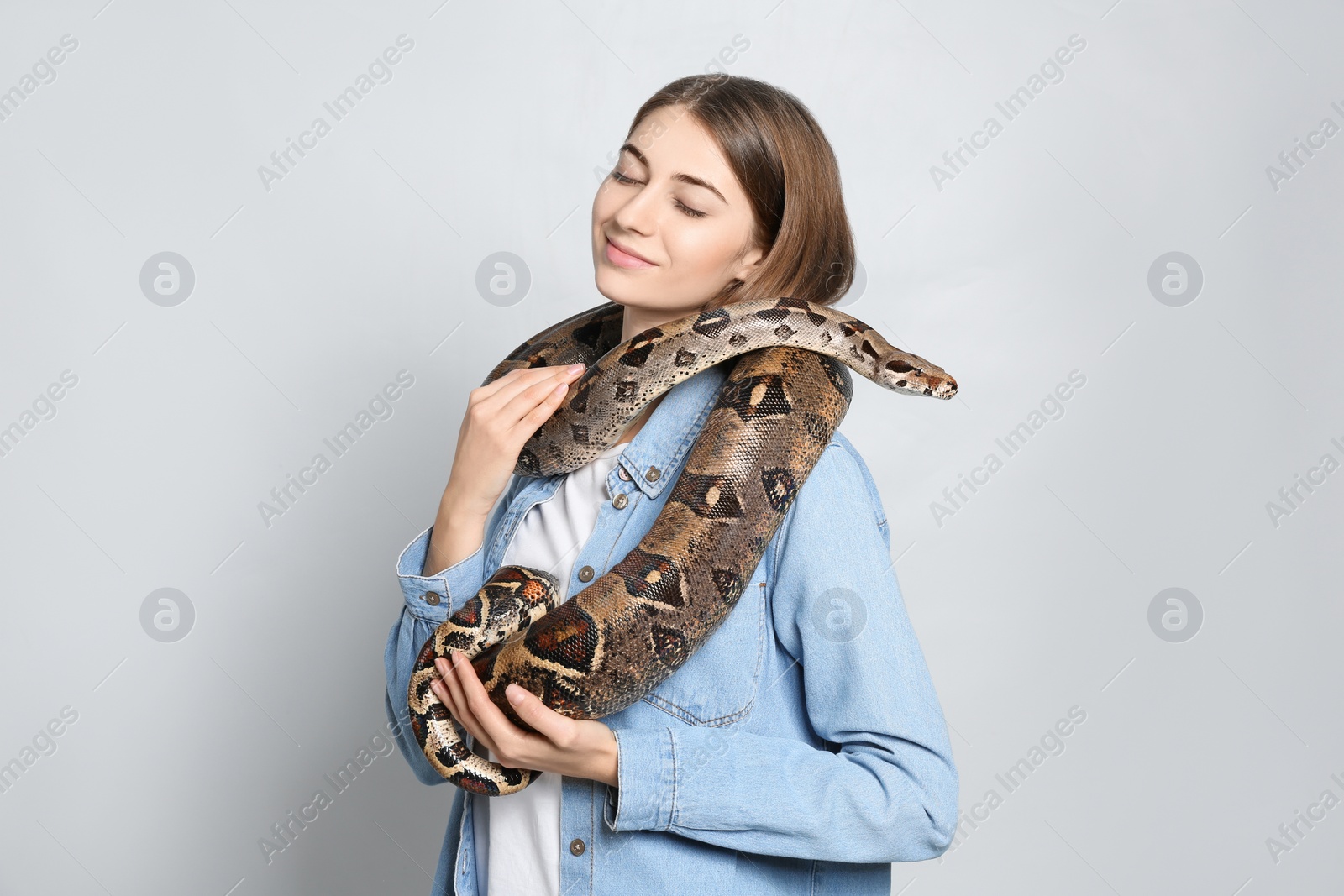 Photo of Young woman with boa constrictor on light background. Exotic pet