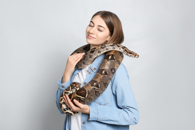 Photo of Young woman with boa constrictor on light background. Exotic pet