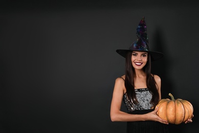 Beautiful woman wearing witch costume with pumpkin for Halloween party on black background, space for text