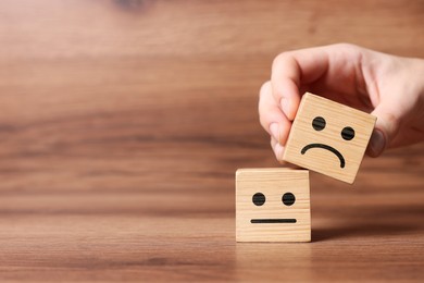 Image of Complaint. Woman choosing cube with drawn sad face instead of another one with happy on wooden table, closeup. Space for text