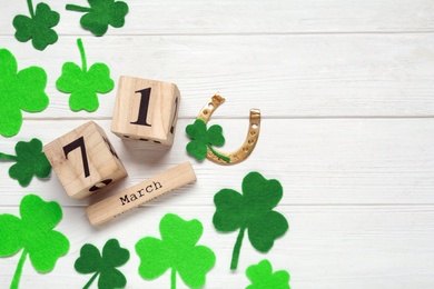 Photo of Flat lay composition with clover leaves and block calendar on white wooden table, space for text. St. Patrick's Day celebration