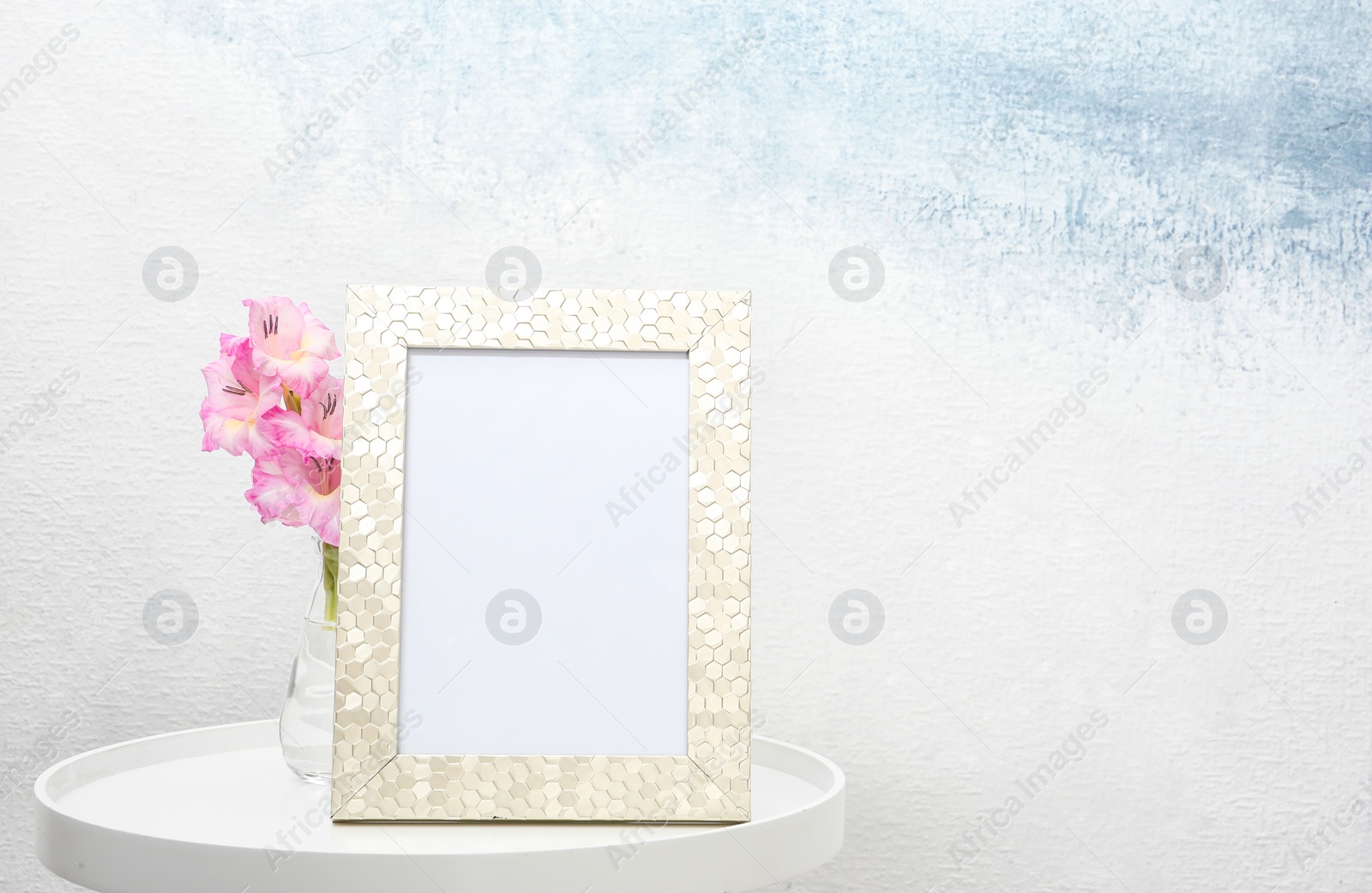 Photo of Blank frame and vase with flowers on table near light wall. Mock up for design