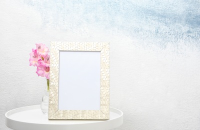 Photo of Blank frame and vase with flowers on table near light wall. Mock up for design