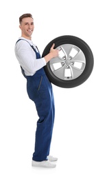 Male mechanic with car tire on white background