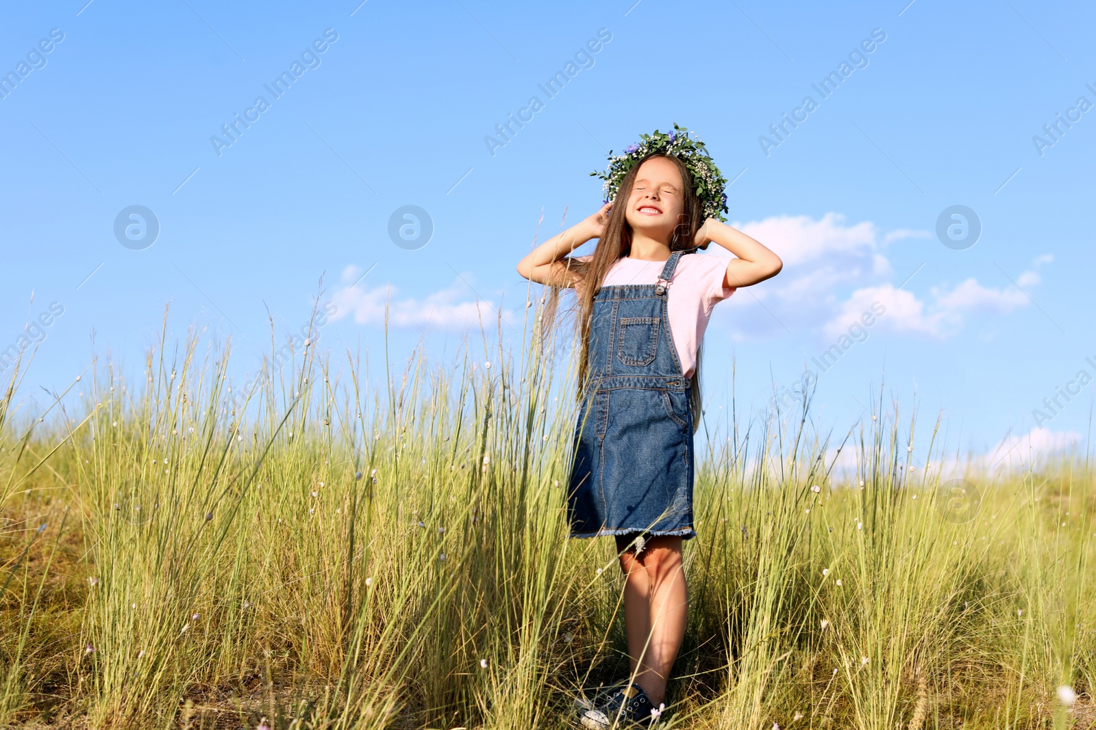 Photo of Cute little girl wearing flower wreath outdoors, space for text. Child spending time in nature