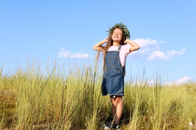 Cute little girl wearing flower wreath outdoors, space for text. Child spending time in nature
