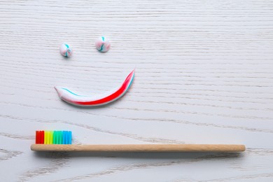 Photo of Funny face made with toothpaste and brush on white wooden background, flat lay
