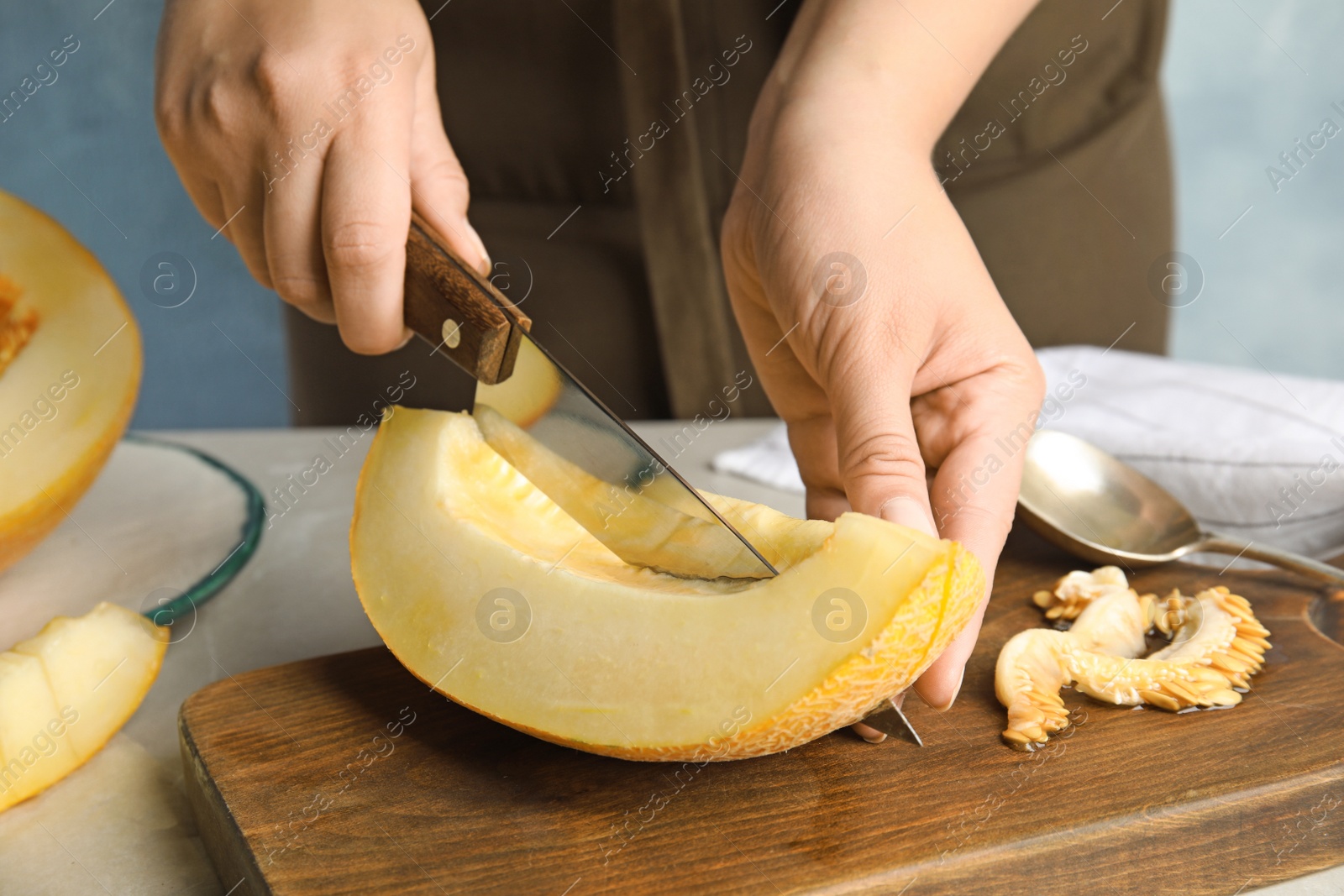 Photo of Young woman cutting ripe melon on board at table, closeup