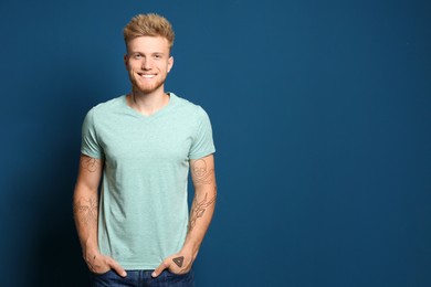 Image of Handsome man with beautiful tattoo sketches on blue background. Space for text