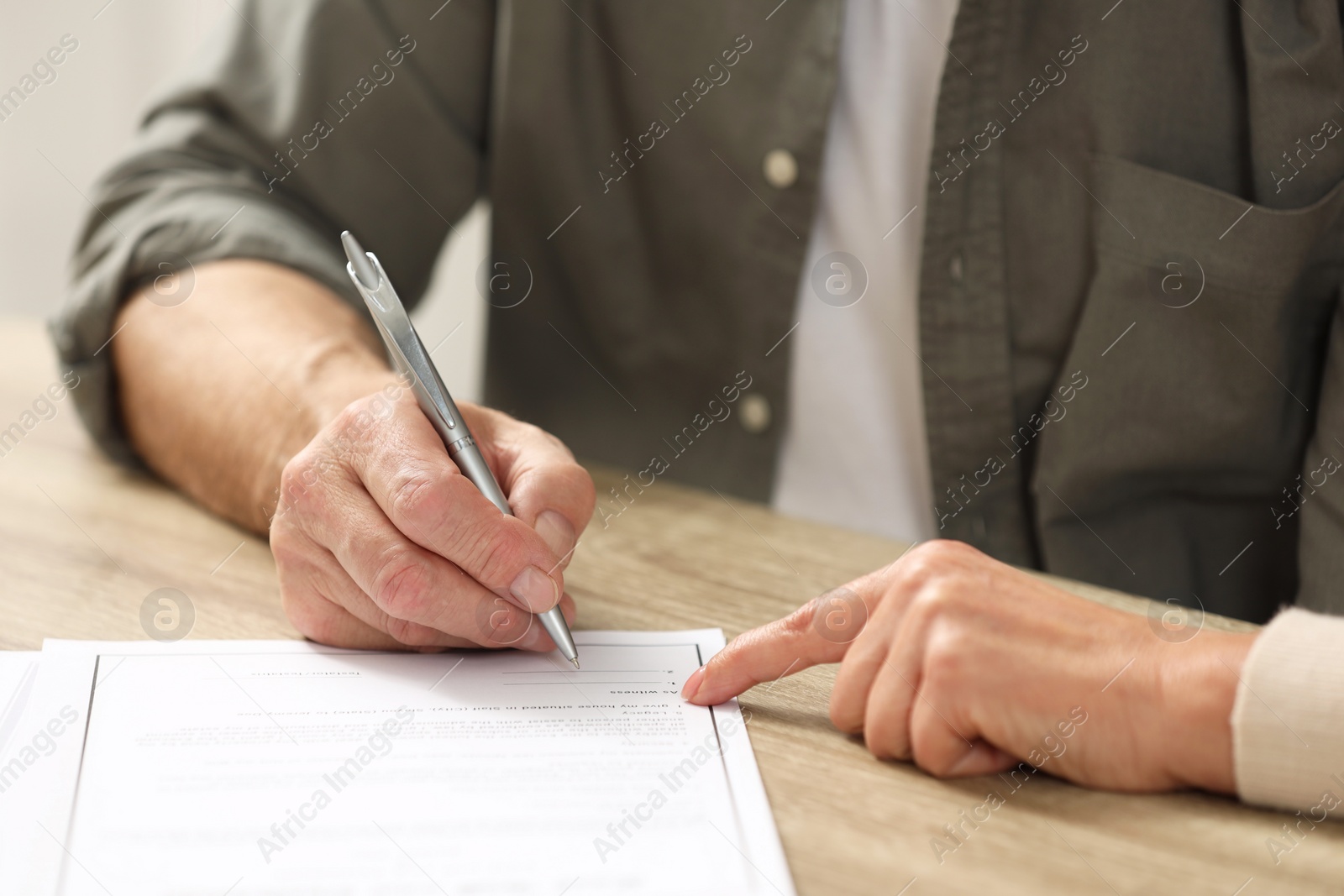 Photo of Notary pointing to senior man where to sign Last Will and Testament at wooden table indoors, closeup