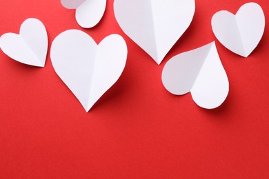 White paper hearts on red background, flat lay. Space for text